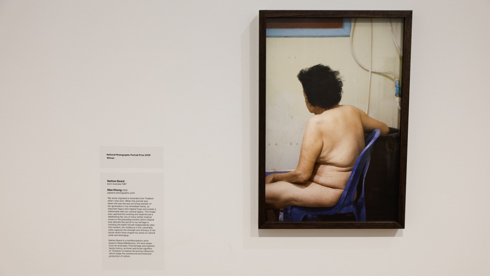 Winning image. Mae Khong 2026 by Nathan Beard. Judges&rsquo; statement: "This photograph of Nathan Beard&rsquo;s aunt Mae Khong has an immediate and compelling emotional pull. Through its tight composition and simple colour palette interspersed with soft blue tones, combined with the vulnerability of a private yet familiar pose, the artist creates a portrait of palpable intimacy. Even though we can&rsquo;t see the subject&rsquo;s face, we are drawn into a connection with her, perhaps sensing the weight of her life experiences or recognising our own loved ones in this quietly captured moment. There is both resilience and fatigue legible in Mae&rsquo;s posture. With water droplets still on her skin, this is a candid scene but it also speaks to the depth of familial connection between artist and subject."The National Photographic Portrait Prize 2026. Image: Tim Levy