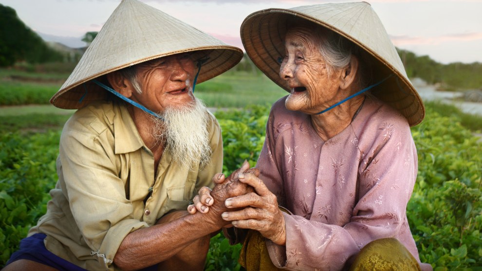 A loving couple in Hoi An, Vietnam, share a moment of joy and happiness together in their garden as the sun sets. This photo was taken in the direct sunlight, however the sun had almost set which is why the quality of light is pleasing &ndash; the shadows are smooth and the sunlight provides some warmth. I asked them to squat down for relaxed body postures but had to make sure the background was uncluttered and as clean as possible, to keep the focus on the couple while still giving a sense of place and their daily environment. Nikon D800, 24-85mm f2.8-4 lens @ 50mm, 1/200s @ f7.1, ISO 500.