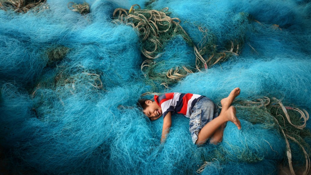 Boy playing in fishing nets in the Mekong Delta region of Vietnam. I found the background of the fishing nets and encouraged the boy to jump into them, and I even demonstrated the idea to him by doing it myself. I noticed that the nets were in a good location that was undercover yet near an opening to the sky for strong, even light, and would make for interesting patterns in a background to this playful environmental portrait taken in Vietnam. Nikon D800, Nikon 24-85mm f2.8-4 lens. 1/250s @ f8, ISO 500.