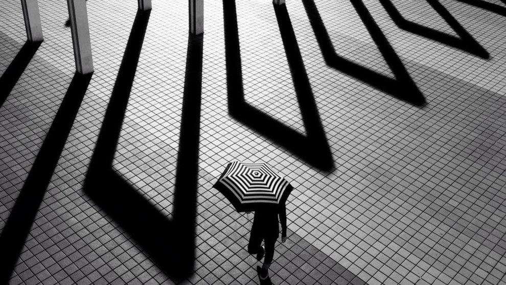 A finalist in the Mobile category &ndash; a woman carrying a striped black and white umbrella passes some gates (Credit: Laurence Bouchard)