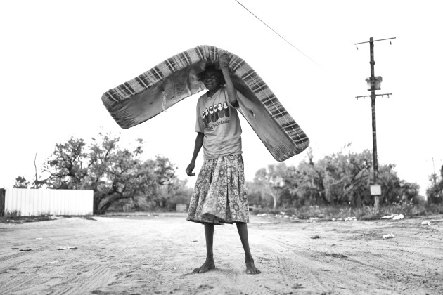 A lack of affordable short-term accommodation, combined with Aboriginal people moving in from remote communities, has led to people camping on bush blocks and parks in town. 
Lydia is moving here mattress to the side of the road. One Mile community, Broome, Western Australia. &copy; Ingetje Tadros.