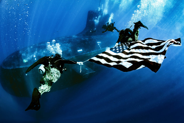 Divers from the USN&rsquo;s Naval Special Warfare Group Eight display the national ensign while underway on Virginia Class fast-attack submarine USS New Mexico (SSN 778). (US Navy)