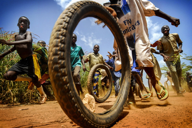 In an impoverished village in the West African state of Togo, a group of children play and run behind old motorcycle tyres in the red dusty dirt outside of an NGO clinic. Grand Prize - Happiness. &copy; Antonio Aragon Renuncio (Spain).