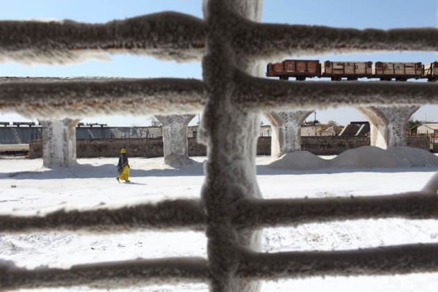 Salt factory, Rajasthan, India. Crusted salt on a window frame as a worker walks to the rail yard. &copy; Brendan Esposito.