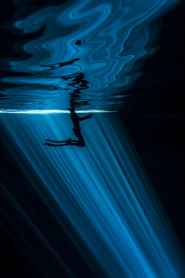 &copy; Wendy Timmermans, Netherlands. WINNER - PRIMARY COLOURS (SINGLE IMAGE CATEGORY). Cenote Nah Yah, Mexico. As freedivers, we explore the abyss on one breath only. Inside the Cenote the water was completely still and silent, but his tiny movements on the surface created an irregular pattern of reflection, beautifully contrasting with the straightness of the rays underwater.