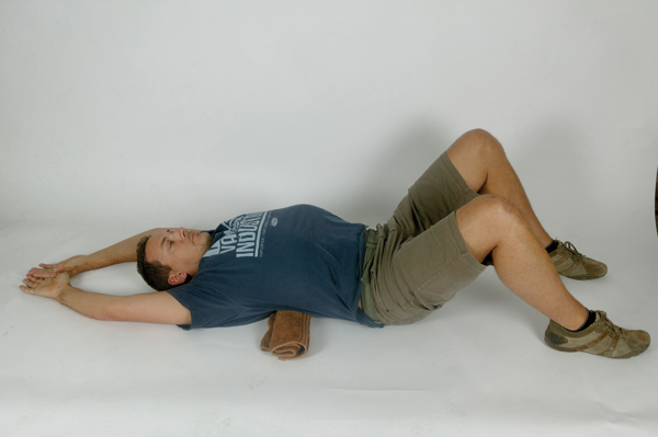 Okay, dropping to the ground underneath your desk may not be viable at the office, but this is a nice passive stretch that shouldn&rsquo;t be too much of an imposition before bed. It is hard to get your head on top of your shoulders, and keep your shoulders back, unless you have good mid-back mobility. This stretch should be a pleasure after a long day tapping the keys (and also after a long day in the saddle for those lucky enough to get out!)
Lay on your back, hips and knees bent, feet on the floor. Have rolled up towel placed crossways underneath your back, in the mid-back (thoracic) area. Lift your arms above your head to rest on the floor. Hold 20 seconds, then repeat with towel in a slightly higher position. Do this one at the end of every day.