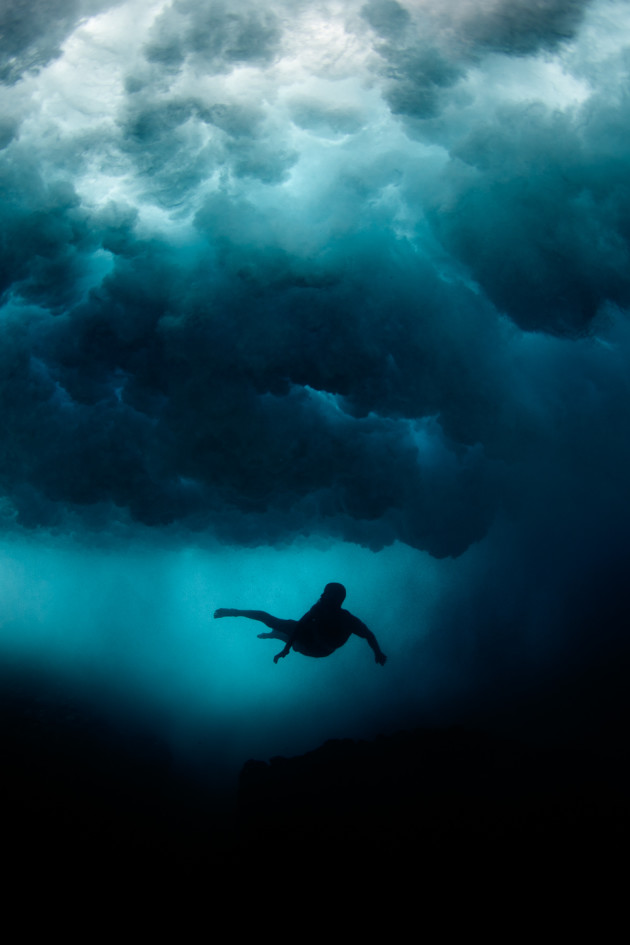&copy; Ed Sloane. A Tahitian swimmer navigates between sizeable waves above and sharp coral below.