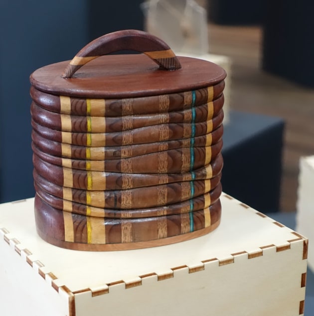 Brian Dawson, Composite Ring Box, jarrah, Huon pine, silky oak, myrtle (Tiny Treasures). 'I aim to present a visually engaging selection of Australian timbers displayed in an unusual and distinctive way. I try to avoid straight lines and rectilinear forms and aim for a sculptural, organic shape with no straight lines and with verticals and horizontals slightly askew to mimic a natural, growing form. The timbers are glued to form a sandwich, bandsawn in an uneven oval and then the central section is removed using a bandsaw. The bandsaw is again used this time to cut horizontally into uneven layers each of which is carefully sanded to form rounded, organic form. The layers are glued together and tops and bottoms are finally  added."