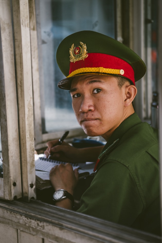 The Crossing Guard:
They say if you can cross the street in Saigon, you can do just about anything. I&rsquo;ve been standing on this corner for what feels like twenty minutes. A Vietnam-visiting rookie exposed by my hesitancy. The trick, they say, is to simply step out onto the road with confidence, that the herd of scooters coming your way will do the rest.
Buying time, I wonder what will happen if I apply this advice and raise my camera, with confidence, towards the guard tower. Perhaps he will take care of the rest?
Image: Francesca Donnoli