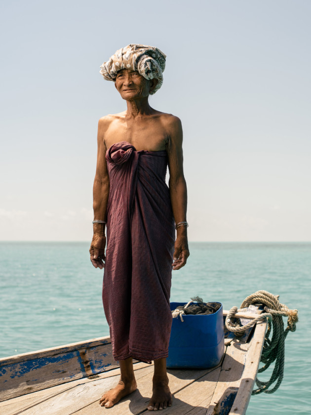 Buggarah, an elderly Bajau Laut woman, stands on her boat off Denawan Island. &copy; Mark Lehn.