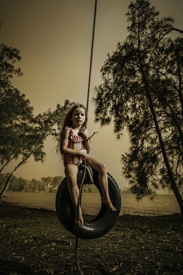 &copy; Shelley Reis. Under Smoky Skies &ndash; &ldquo;For NSW, the Summer of 2020 was like no other. Day in, day out, smoke collected on
the horizon creating an eery, orange glow. Over time we grew accustomed to life under smokey skies and our
children adapted to the &lsquo;new normal&rsquo;. This image was shot on the south coast as my daughter, Lola, played on the tyre swing and the ominous glow from with the Currowan fire illuminated the background.&rdquo;