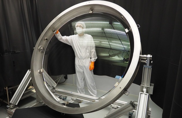 A technician seen through the human-sized L1 lens of the Rubin Observatory camera. Image: LSST