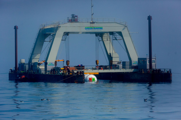 Project Natick&rsquo;s Northern Isles data centre is partially submerged and cradled by winches and cranes between the pontoons of an industrial catamaran-like gantry barge. At the deployment site, a cable containing fiber optic and power wiring was attached to the Microsoft data centre, and then the data centre and cable lowered foot-by-foot 117 feet to the seafloor. Photo by Scott Eklund/Red Box Pictures.