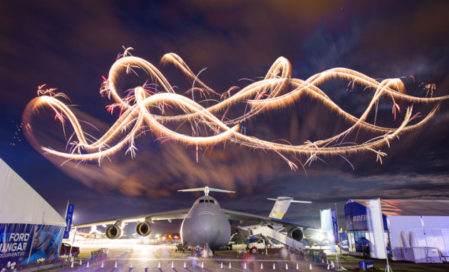 Night aerobatics paint the night sky above a US Air Force C5 Galaxy at Airventure 2019. (Chris Miller / Experimental Aircraft Association)