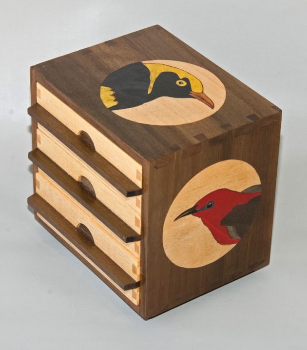 First prize winner, Tiny Treasures, Robin Cromer, ACT. Queensland Tribute, Qld walnut veneer, silver ash. "Maleny is pure Queensland so a tribute to the state seemed to be an appropriate for this small drawer unit. Three iconic symbols of the state were featured in marquetry: The regent bowerbird, the scarlet honeyeater and the Cooktown orchid. 
The timbers also had to represent Queensland so some Queensland walnut (recycled) and silver ash were used. The drawers are lined in black suede pigskin and were made relatively 'loose' to allow for expansion as the piece would travel from a dry Canberra environment to a more humid one in Queensland."
The back of the piece and the underside of the drawers&rsquo; feature figured Queensland walnut veneer; as the 'show side' of shop-made three-ply (1.8 mm thick).